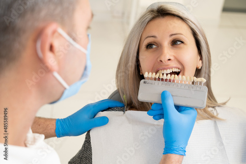Dentist checks color on patient's teeth color chart before implantation procedure in dental clinic.
