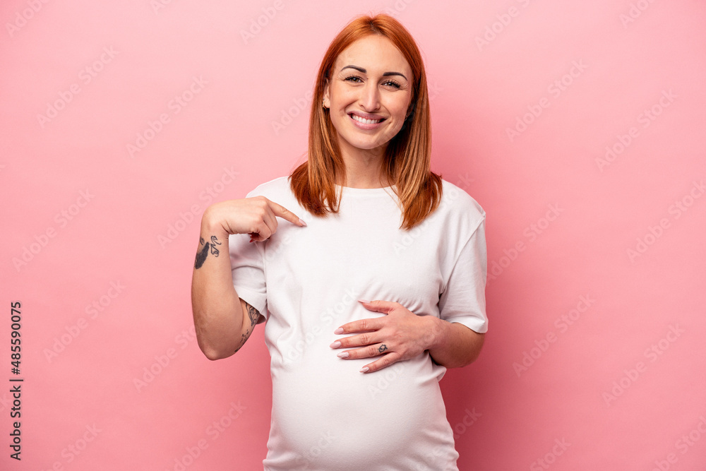 Young caucasian pregnant woman isolated on pink background person pointing by hand to a shirt copy space, proud and confident Young caucasian pregnant woman isolated on pink background person pointing by hand to a shirt copy space, proud and confident