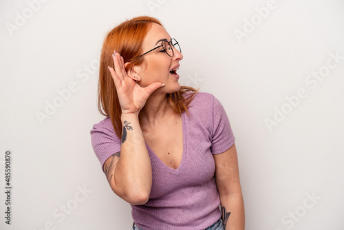 Young caucasian woman isolated on white background trying to listening a gossip.