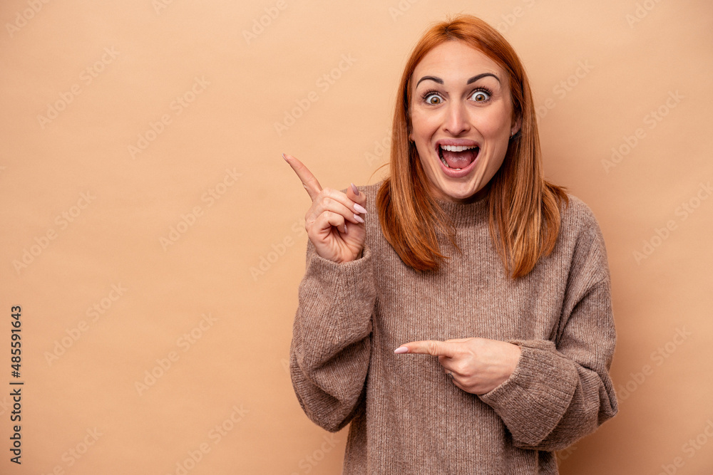 Young caucasian woman isolated on beige background excited pointing with forefingers away.