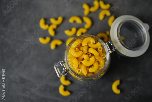 raw macaroni pasta in glass jar on black background 
