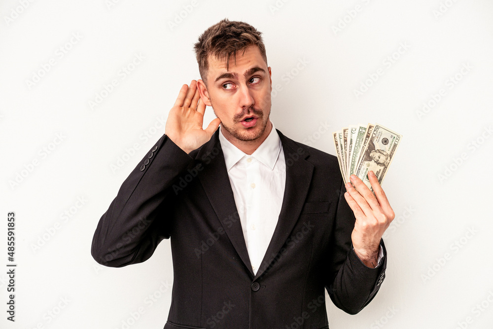 Young caucasian business man holding bank notes isolated on white background trying to listening a gossip. Young caucasian business man holding bank notes isolated on white background trying to listening a gossip.
