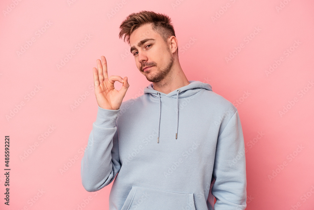 Young caucasian man isolated on pink background winks an eye and holds an okay gesture with hand. Young caucasian man isolated on pink background winks an eye and holds an okay gesture with hand.