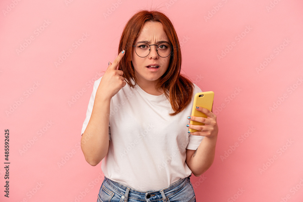 Young caucasian woman holding a mobile phone isolated on pink background showing a disappointment gesture with forefinger. Young caucasian woman holding a mobile phone isolated on pink background showing a disappointment gesture with forefinger.