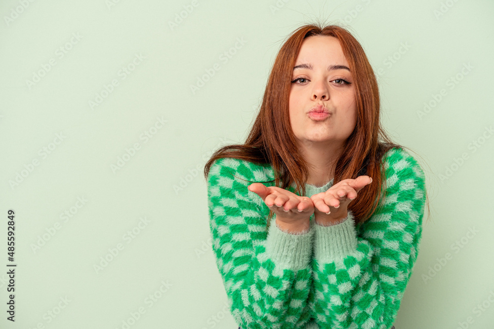 Young caucasian woman isolated on green background folding lips and holding palms to send air kiss. Young caucasian woman isolated on green background folding lips and holding palms to send air kiss.