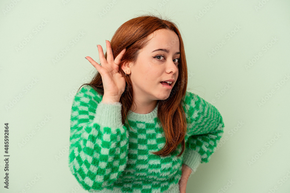 Young caucasian woman isolated on green background trying to listening a gossip. Young caucasian woman isolated on green background trying to listening a gossip.