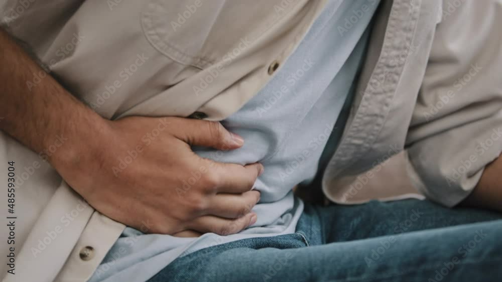 Close-up unrecognizable man feels pain in stomach bend over male hands holding belly by side bad digestive problems concept. Guy has abdominal pain illness suffers liver damage ache unwell poisoning Close-up unrecognizable man feels pain in stomach bend over male hands holding belly by side bad digestive problems concept. Guy has abdominal pain illness suffers liver damage ache unwell poisoning