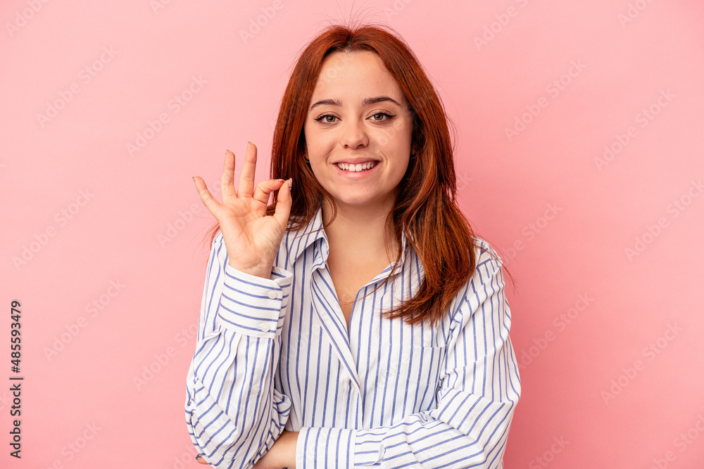 Young caucasian woman isolated on pink background winks an eye and holds an okay gesture with hand. Young caucasian woman isolated on pink background winks an eye and holds an okay gesture with hand.