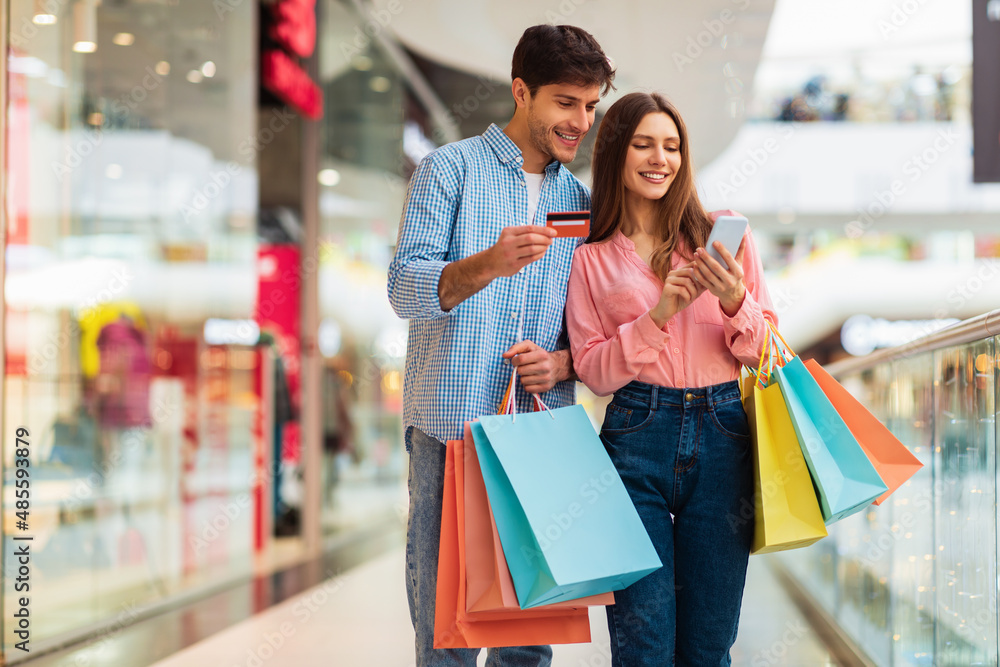 Happy Couple Shopping Using Smartphone And Credit Card In Mall Happy Couple Shopping Using Smartphone And Credit Card In Mall