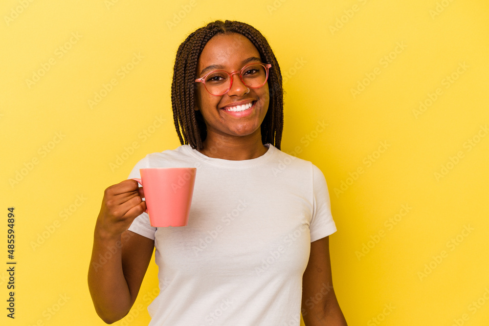 Young african american woman holding a mug isolated on yellow background happy, smiling and cheerful. Young african american woman holding a mug isolated on yellow background happy, smiling and cheerful.