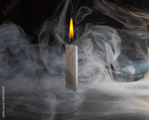 a brightly burning candle surrounded by smoke, on a dark background.