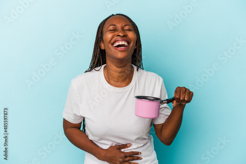 Young african american woman holding pan isolated on blue background laughing and having fun.