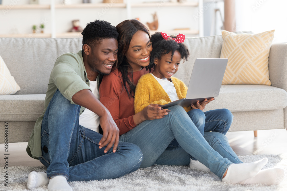 Happy african american family of three relaxing with laptop at home