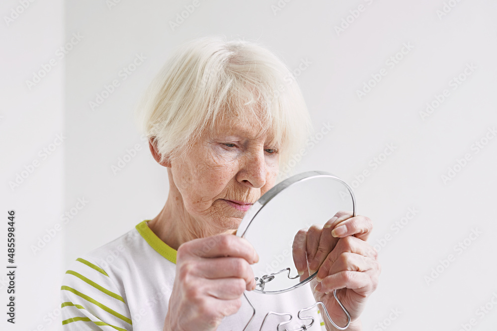 senior sad woman looking at herself in mirror. Age, time, skin care concept senior sad woman looking at herself in mirror. Age, time, skin care concept