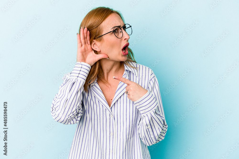 Young caucasian woman isolated on blue background trying to listening a gossip. Young caucasian woman isolated on blue background trying to listening a gossip.
