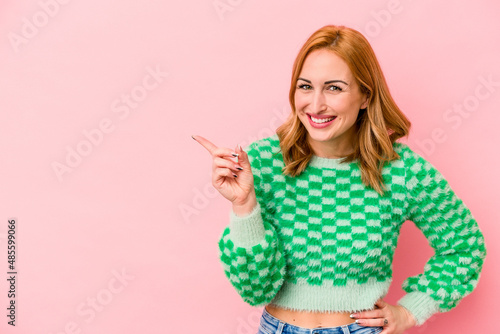 Young caucasian woman isolated on pink background smiling cheerfully pointing with forefinger away.