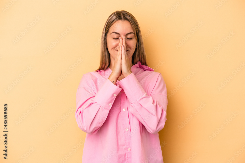 Young caucasian woman isolated on yellow background holding hands in pray near mouth, feels confident. Young caucasian woman isolated on yellow background holding hands in pray near mouth, feels confident.