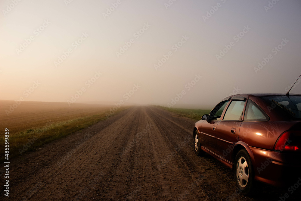 Asphalt road with a parked car in the morning mist on the background of dawn.