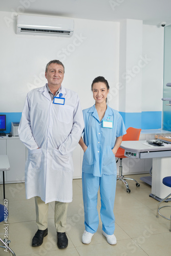 Team of smiling ophthalmologist and his assistant standing in medical office