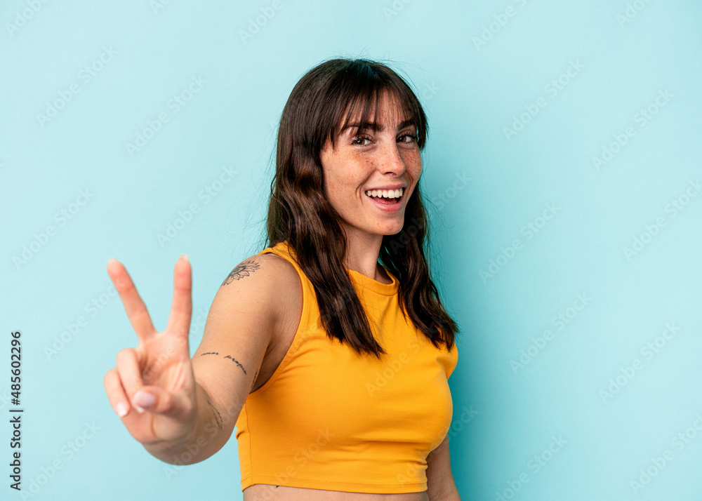 Young Argentinian woman isolated on blue background joyful and carefree showing a peace symbol with fingers. Young Argentinian woman isolated on blue background joyful and carefree showing a peace symbol with fingers.