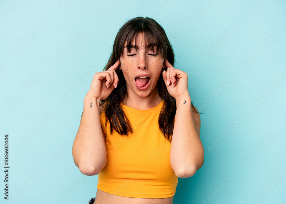 Young Argentinian woman isolated on blue background covering ears with fingers, stressed and desperate by a loudly ambient. Young Argentinian woman isolated on blue background covering ears with fingers, stressed and desperate by a loudly ambient.