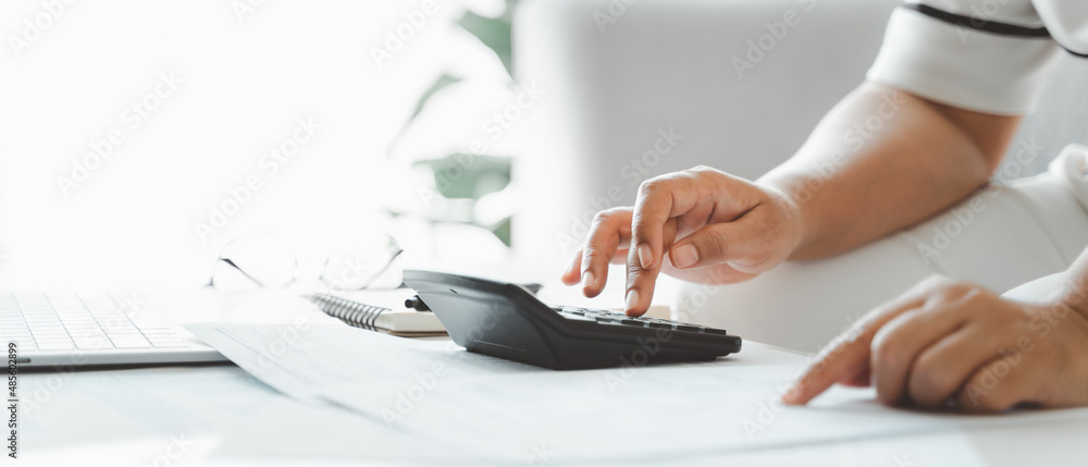 Woman is calculating annual tax, monthly expenses with calculator and filling form of Individual Income Tax Return. Season to pay Tax and Budget planning concept. - obrazy, fototapety, plakaty 