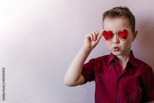 Little boy in glasses with red hearts and a burgundy shirt  air kiss.