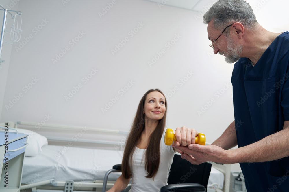 Woman with disability lifting one dumbbell supported by kinesiologist Woman with disability lifting one dumbbell supported by kinesiologist