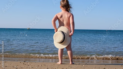 funny little girl 3 years old with a straw hat looks at the sea, back view, close-up. Childhood, relationship, summer vacation concept. selective focus on the hat