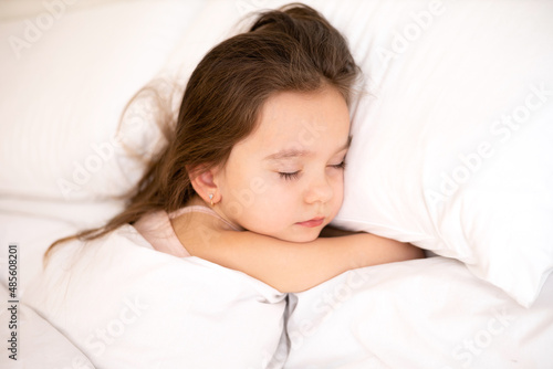 A cute pretty little girl sleeps on a white pillow. Morning. Bedroom. Lifestyle.