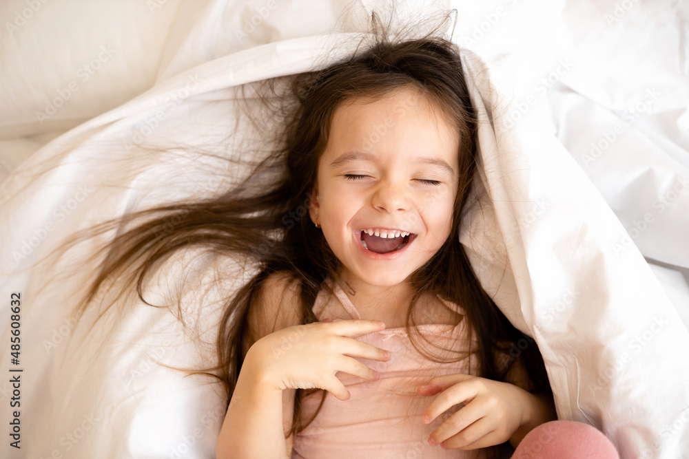 A little funny pretty girl laughs lying on the bed with disheveled hair. Joy. Lifestyle emotions. A little funny pretty girl laughs lying on the bed with disheveled hair. Joy. Lifestyle emotions.