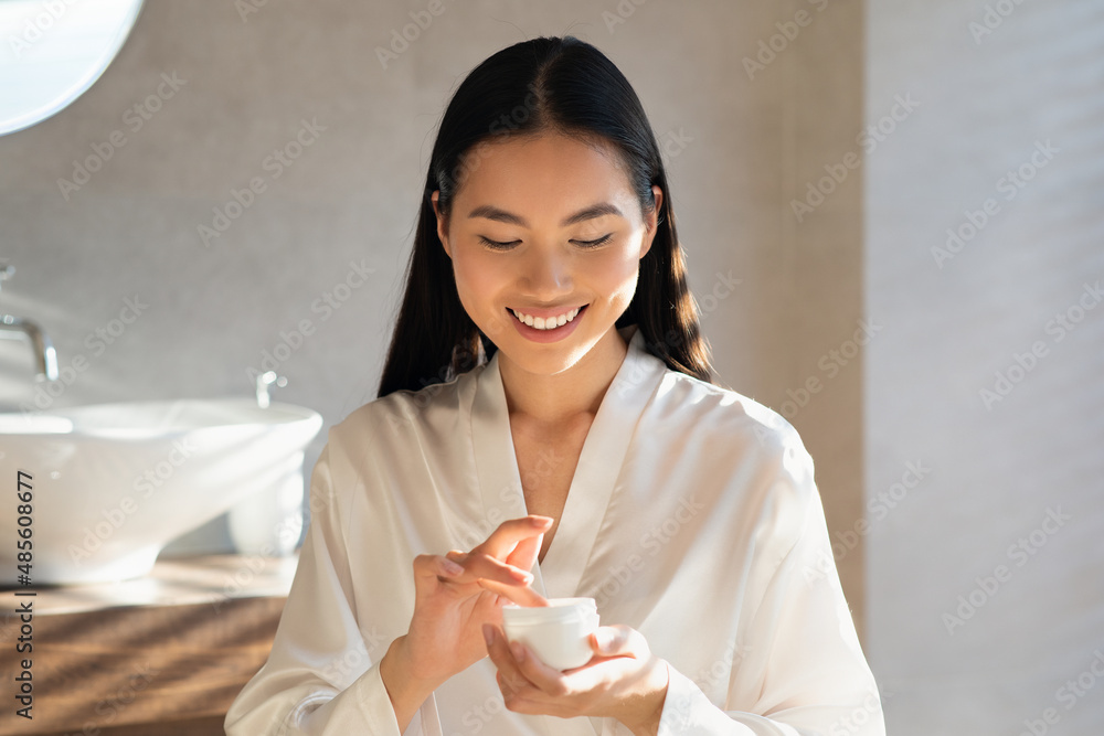 Smiling young asian lady holding jar with beauty product Smiling young asian lady holding jar with beauty product