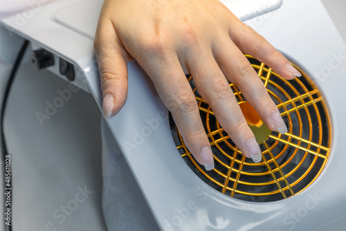 Close-up of a woman's hand lying on a desktop extractor hood for hardware manicure. First stage of nail preparation for applying gel polish is over