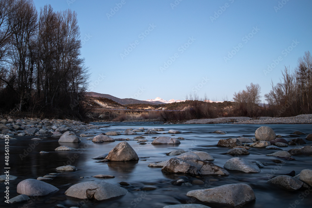 River with rocks and mountains in the background blue sky and some trees in winter long exposure