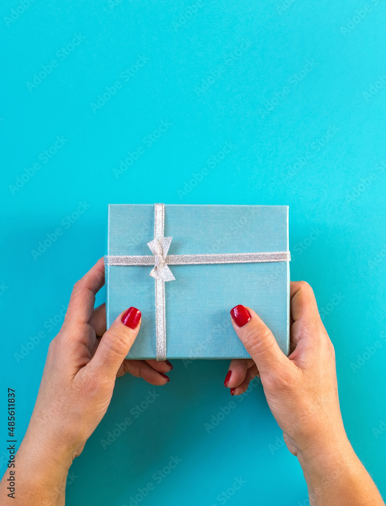 Woman hands holding gift, blue background. Woman hands holding gift, blue background.