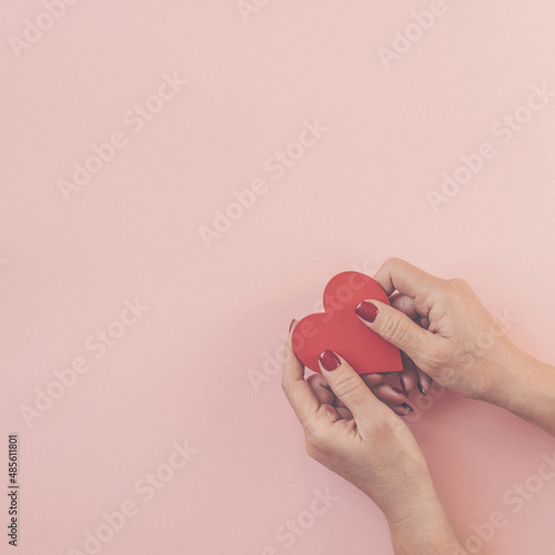 Woman hands holding heart on pink background.