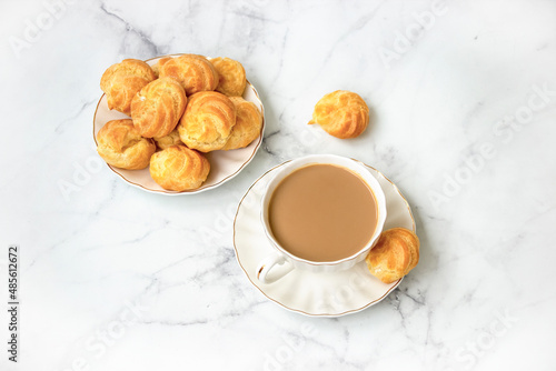 Homemade profiteroles stuffed with whipped cream and milk tea. On a marble light background. View from above.