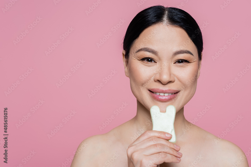 Smiling asian woman with naked shoulders holding jade stone isolated on pink Smiling asian woman with naked shoulders holding jade stone isolated on pink