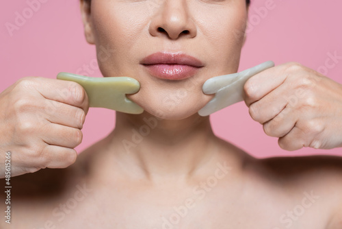 Cropped view of woman massaging chin with jade stones isolated on pink