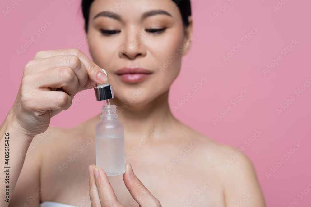 Bottle of serum in hands of blurred asian woman isolated on pink Bottle of serum in hands of blurred asian woman isolated on pink