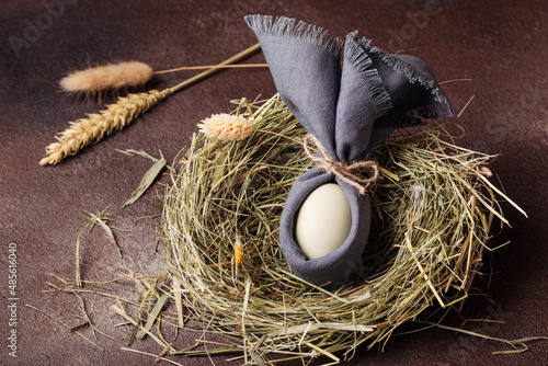 Easter egg decorated like a bunny in a grass nest on a brown background photo