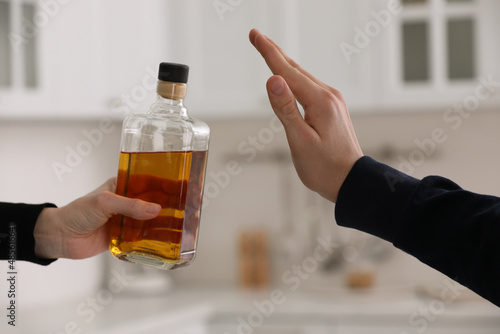 Man refusing to drink whiskey in kitchen, closeup. Alcohol addiction treatment