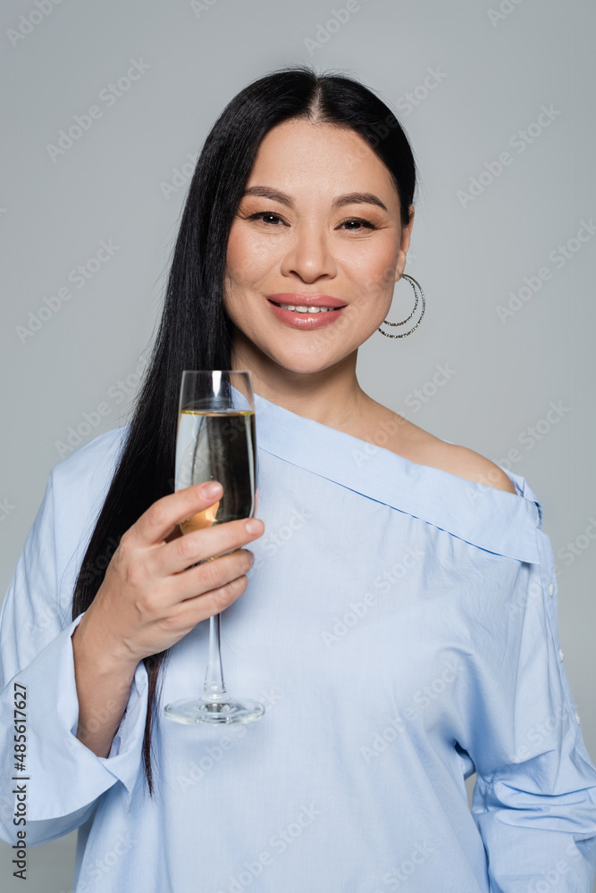 Smiling asian woman in blouse holding glass of champagne isolated on grey Smiling asian woman in blouse holding glass of champagne isolated on grey