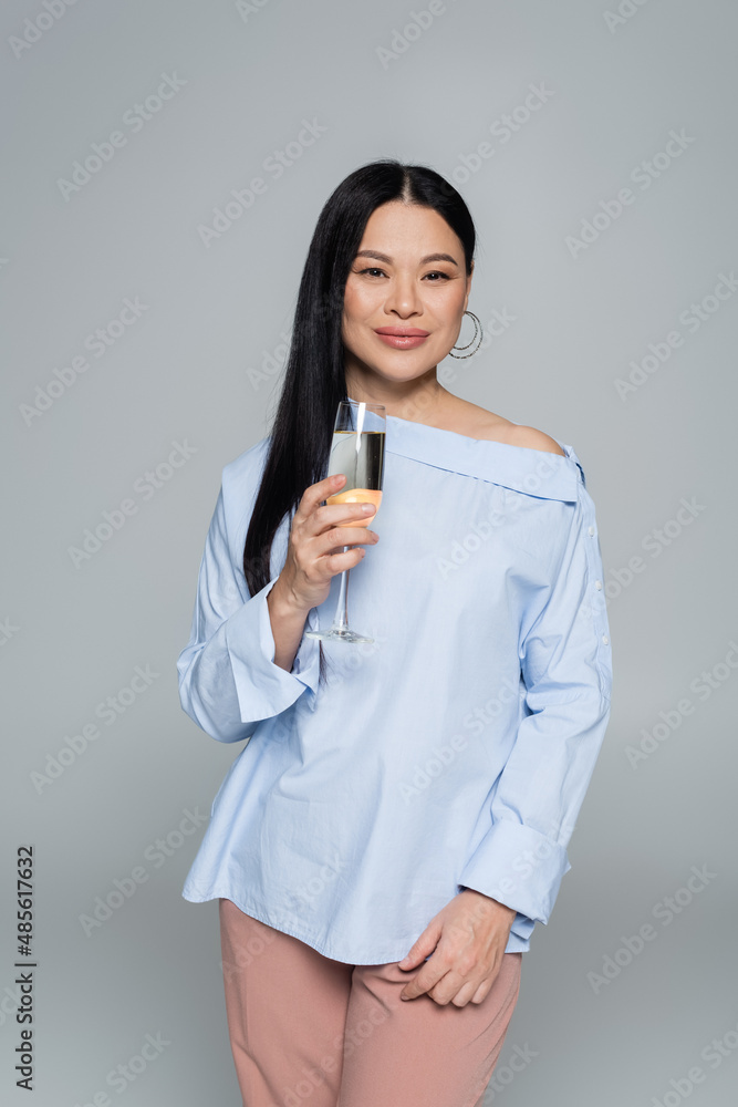 Stylish asian woman holding glass of champagne and smiling isolated on grey Stylish asian woman holding glass of champagne and smiling isolated on grey