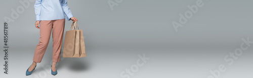 Cropped view of trendy woman holding shopping bags on grey background, banner