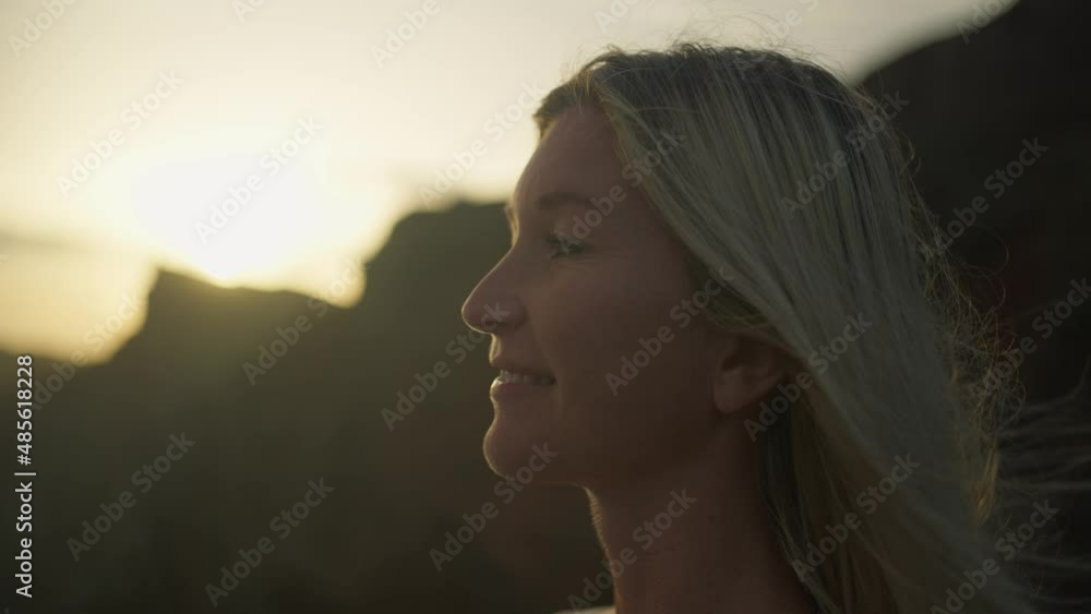 Smiling blond woman enjoying morning sun rays on face, standing on cliff viewpoint, close up Smiling blond woman enjoying morning sun rays on face, standing on cliff viewpoint, close up