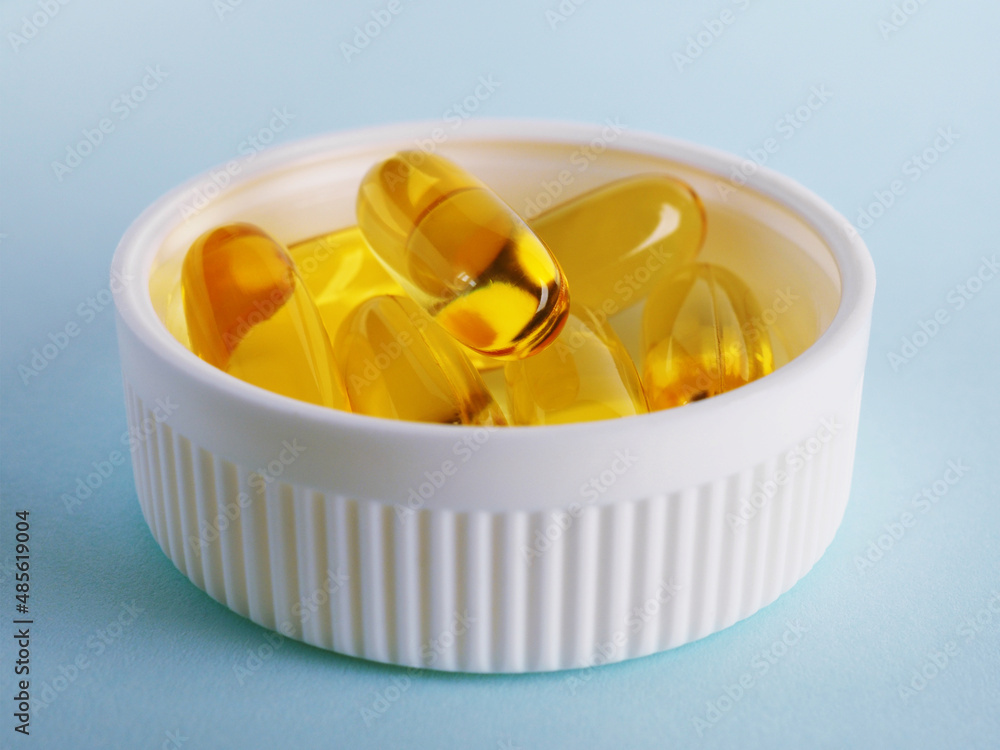 Fish oil. Yellow softgels are in a white bottle cap. Light blue surface