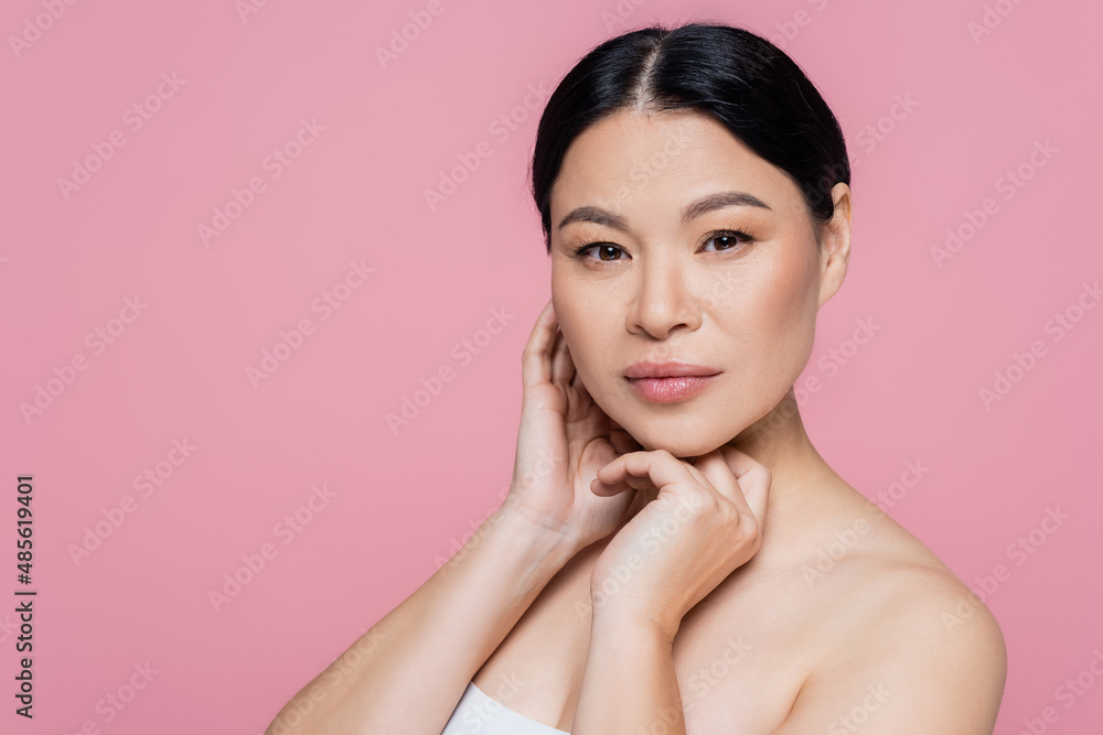 Asian woman with naked shoulder looking at camera isolated on pink Asian woman with naked shoulder looking at camera isolated on pink