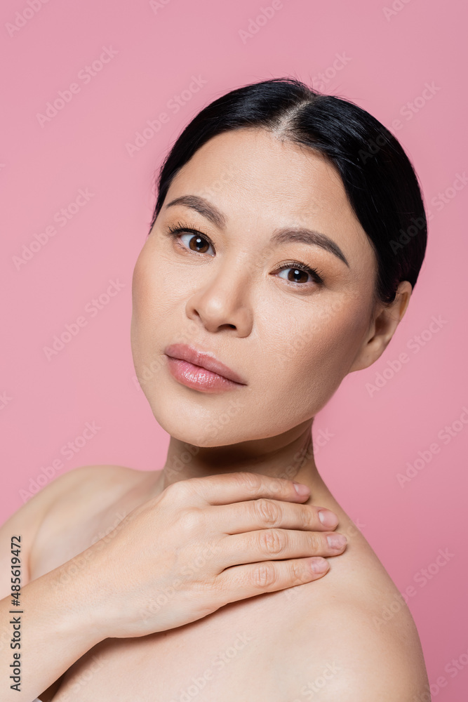 Brunette asian woman touching naked shoulder and looking at camera isolated on pink Brunette asian woman touching naked shoulder and looking at camera isolated on pink