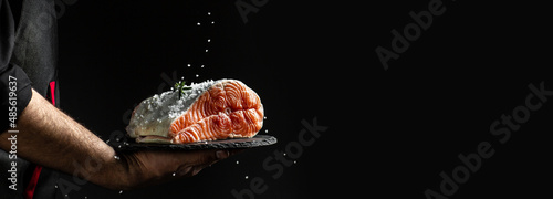 chef prepares salmon steak, process of sprinkling with spices and salt in a freeze motion, marinating salmon fish, adds herbs, seasoning. Long banner format, top view